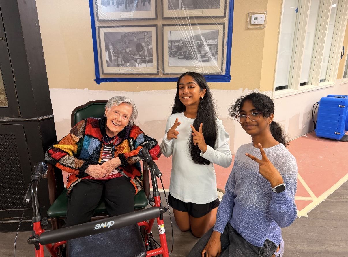 A GrandPals volunteer and two friends smiling with a senior resident during a visit