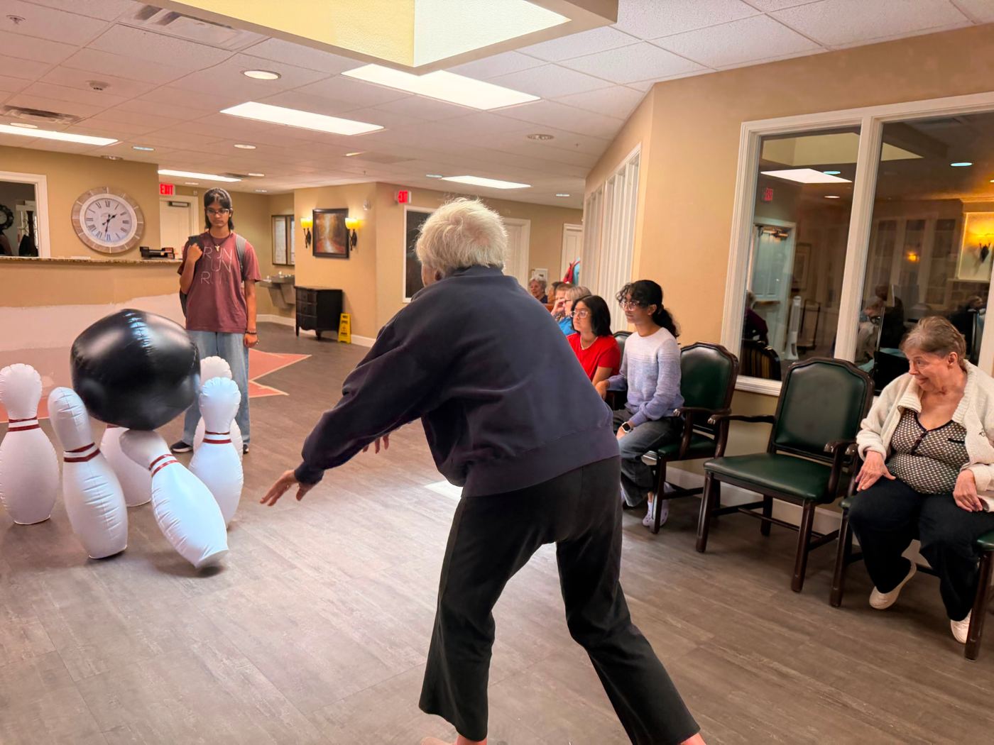 A senior resident bowling with inflatable pins while volunteers cheer on